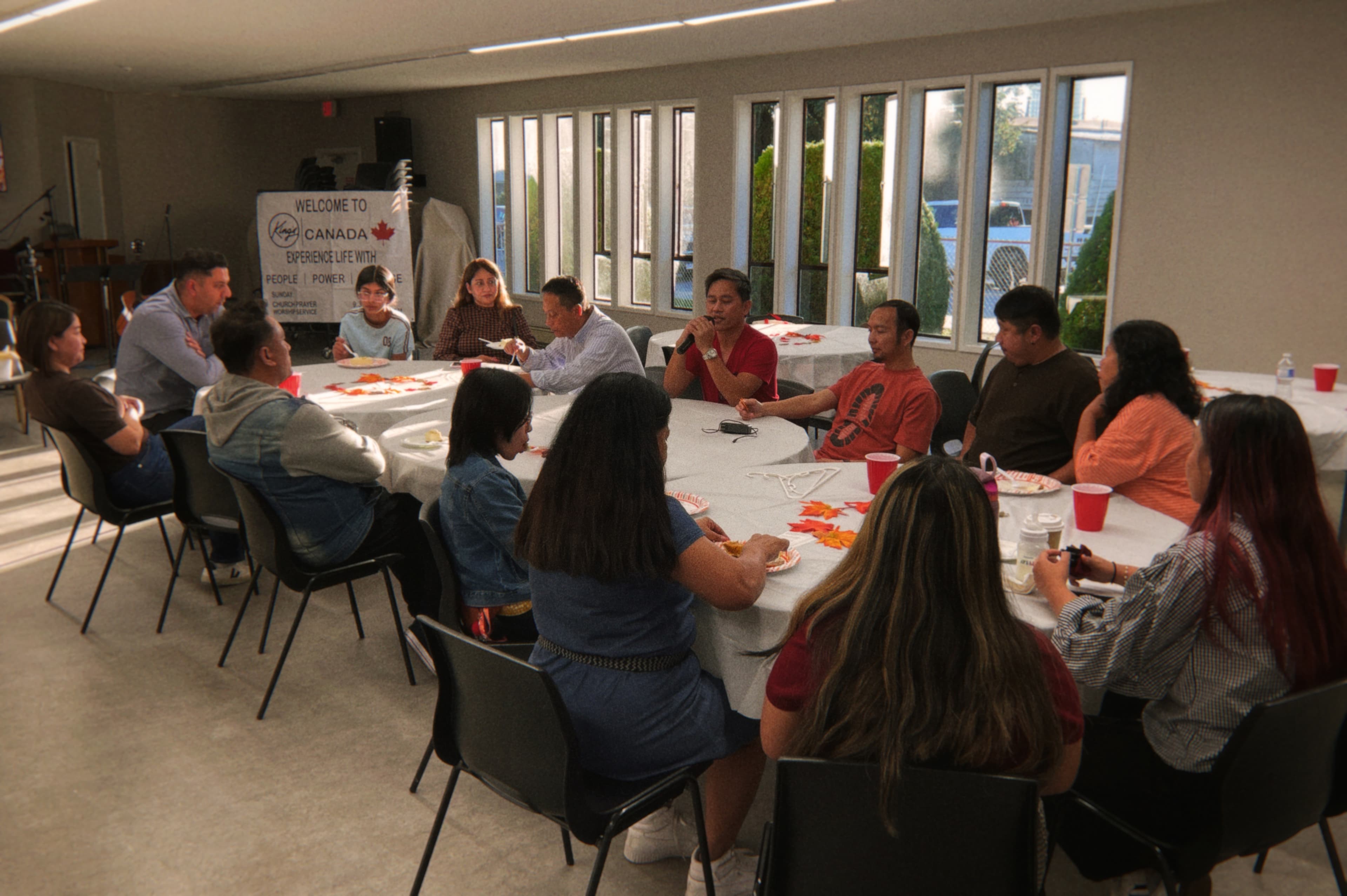 People seated around tables, with one person holding a microphone
